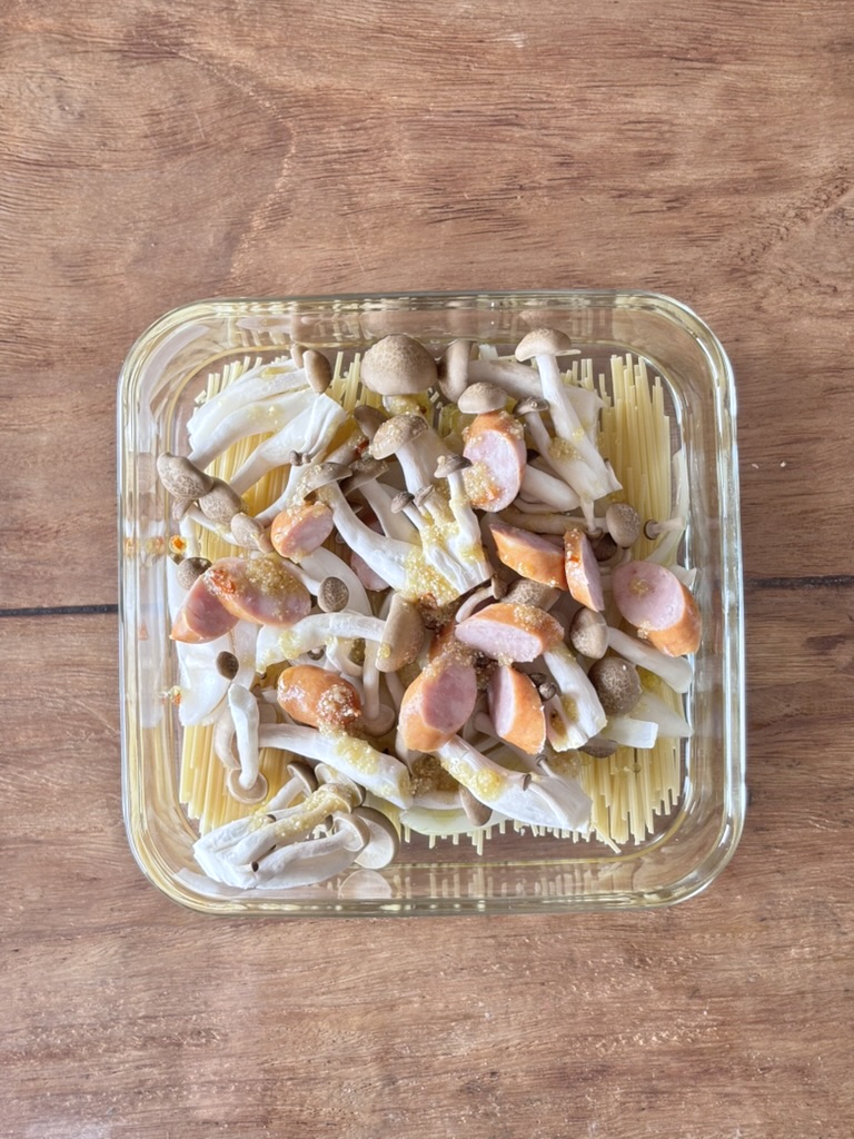 パスタの上に玉ねぎ、ウインナー、しめじ、調味料を乗せる